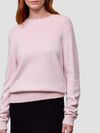 Person wearing a light pink cashmere sweater against a plain background