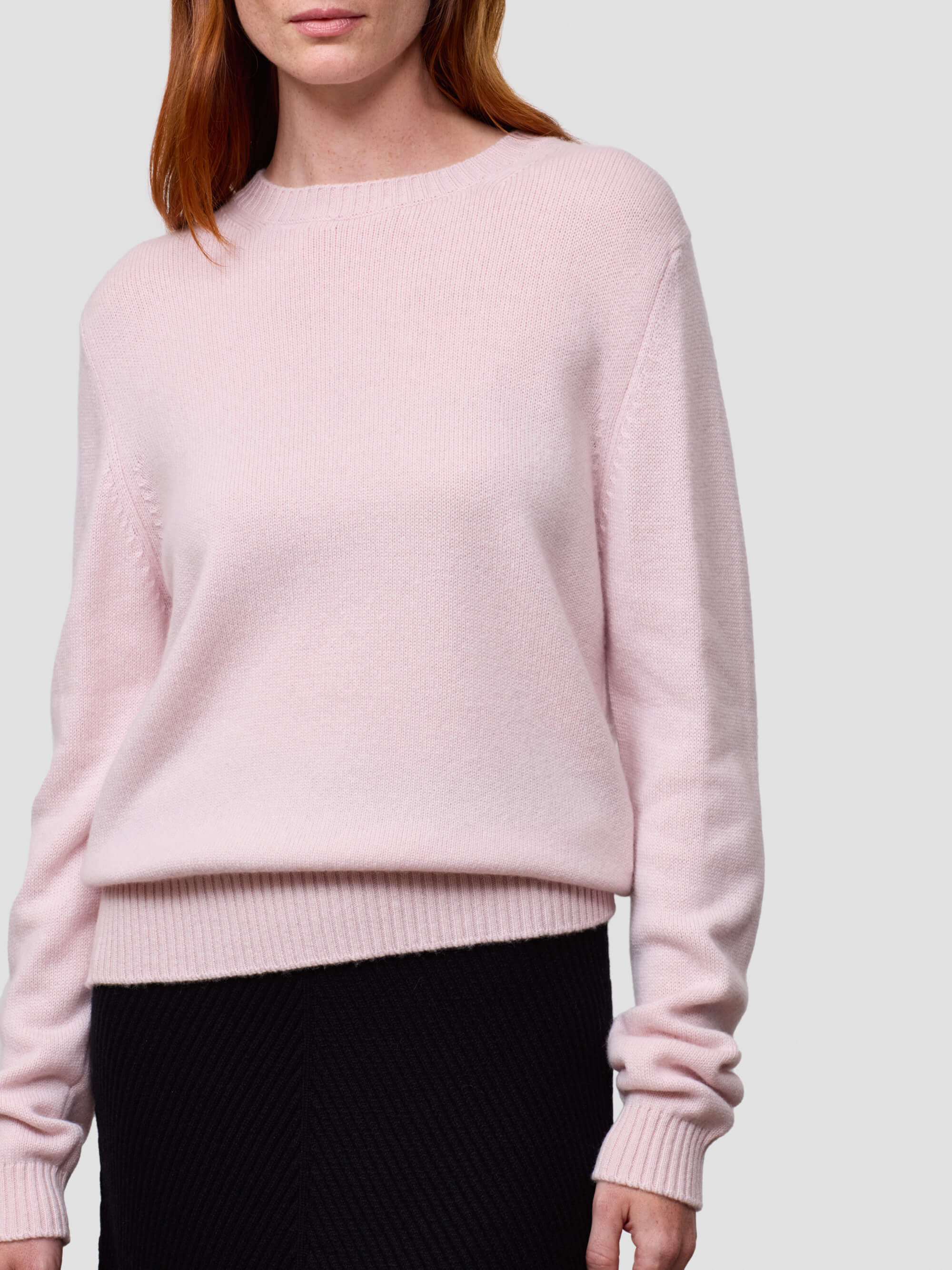 Person wearing a light pink cashmere sweater against a plain background