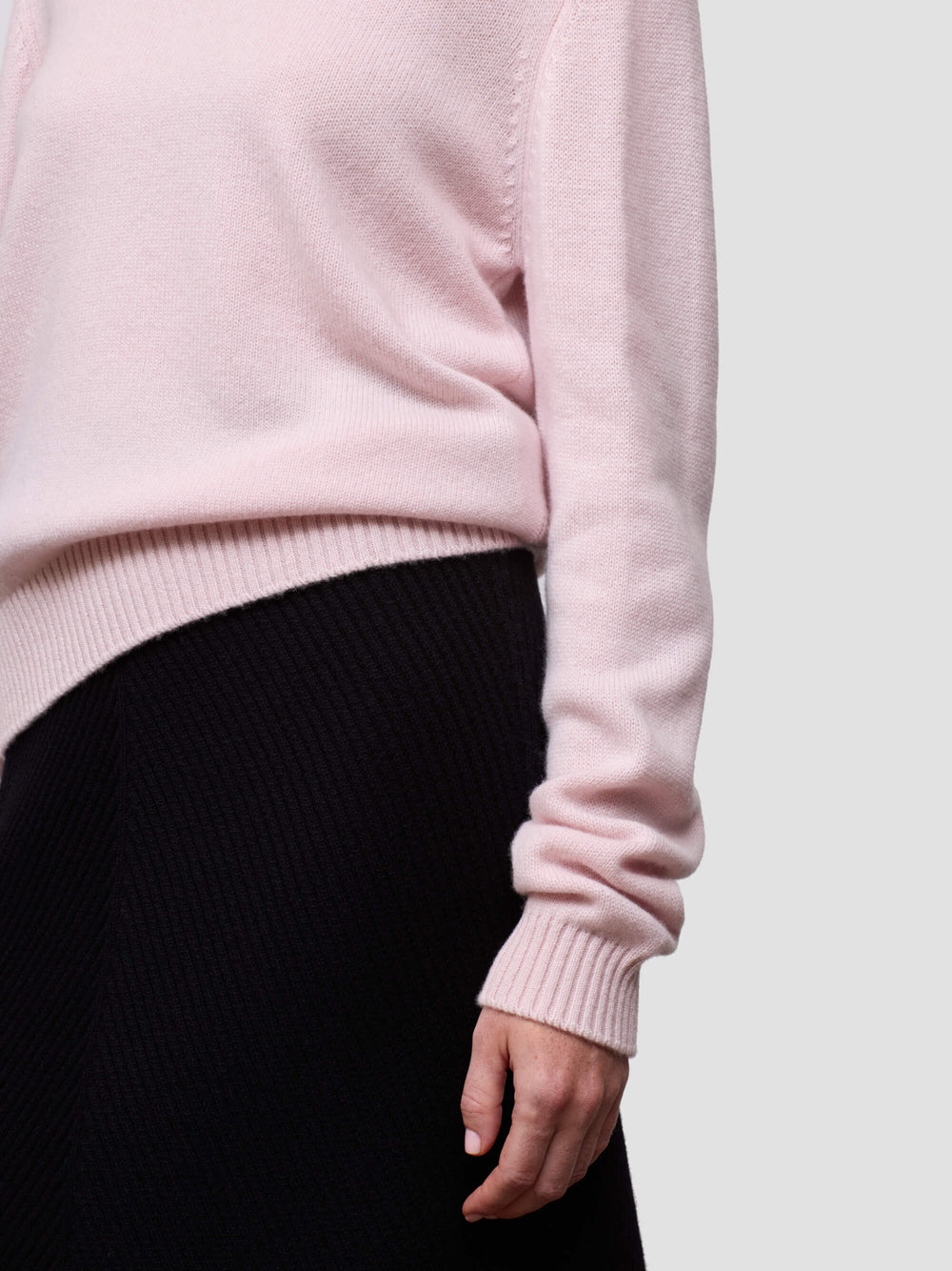 Close-up of a pink cashmere sweater sleeve and black pants against a light gray background