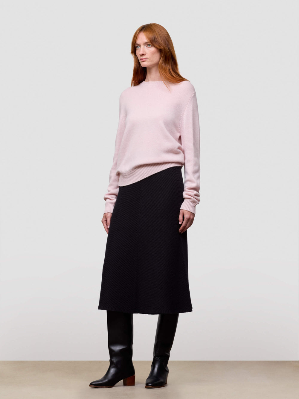 Woman wearing a pink cashmere sweater and black skirt on a white background