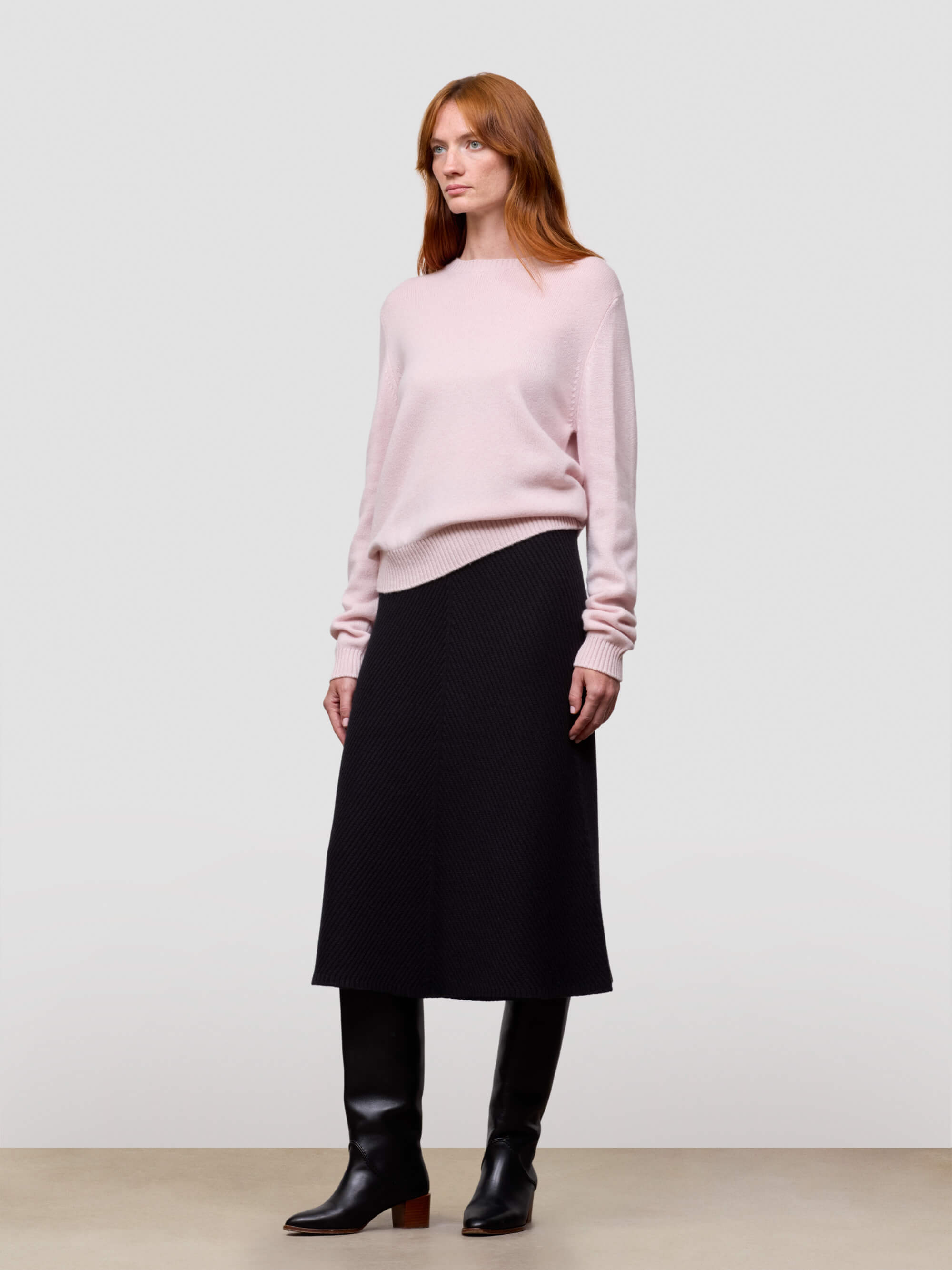 Woman wearing a pink cashmere sweater and black skirt on a white background