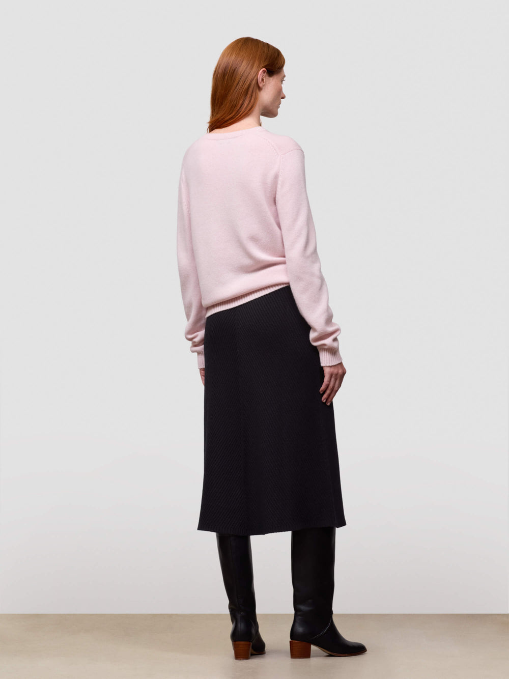 Woman wearing a pink cashmere sweater and black skirt against a white background